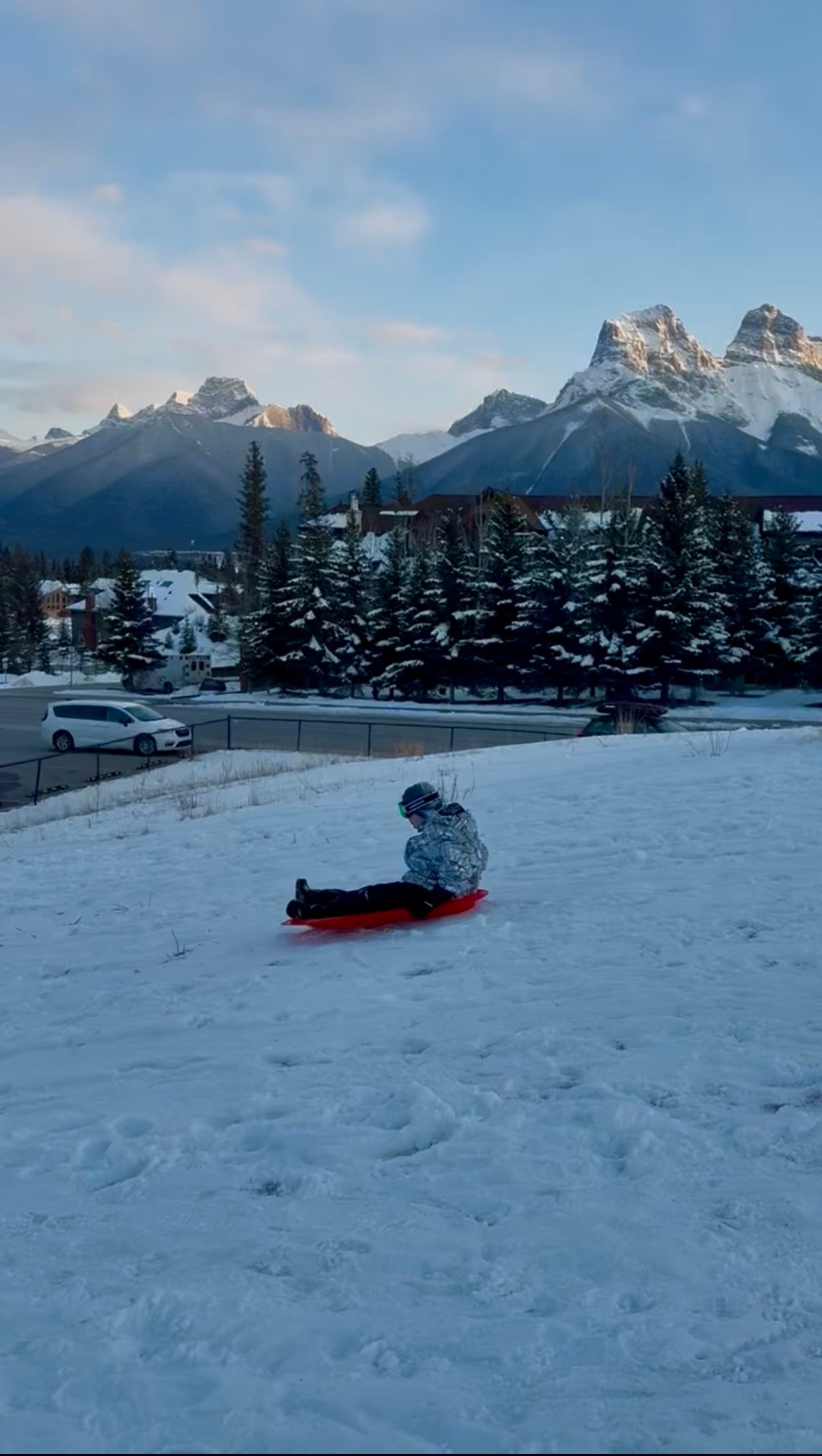 boy sledding down the Canmore Sledding Hill with the Canadian Rockies behind him